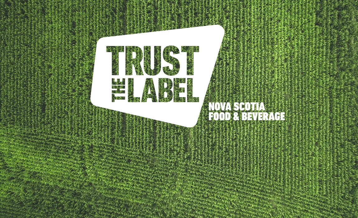 A 'Trust the Label' Nova Scotia Food and Beverage logo overlaid on an aerial photo of a green field of crops