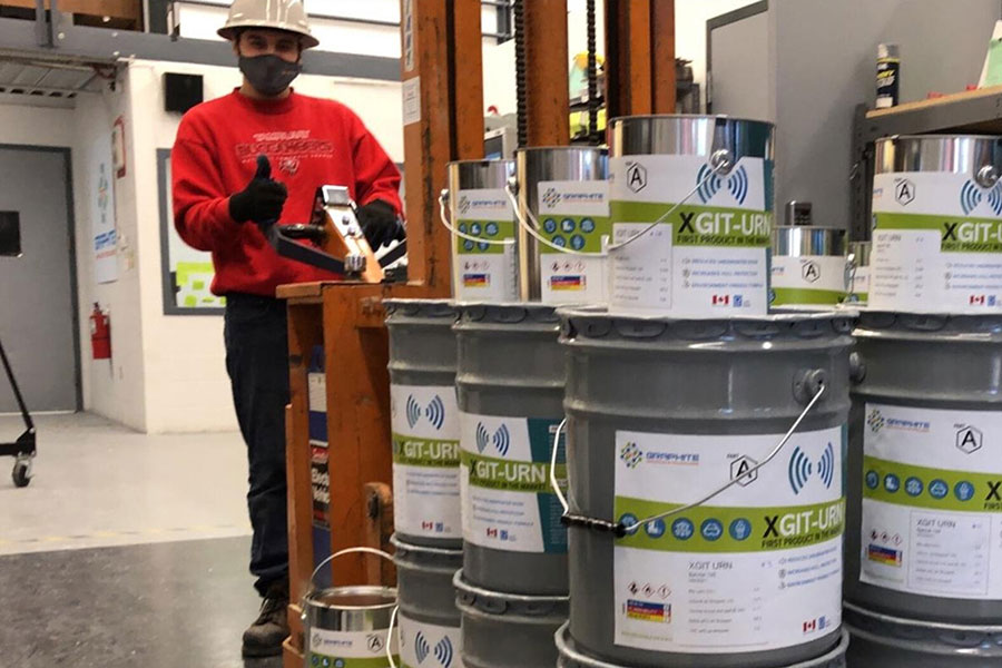 Worker standing behind stacked cans of Graphite Innovation & Technologies product