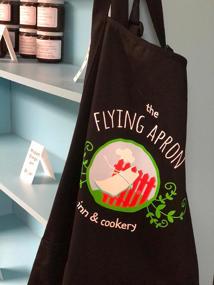 A black apron featuring the logo of The Flying Apron Inn and Cookery.