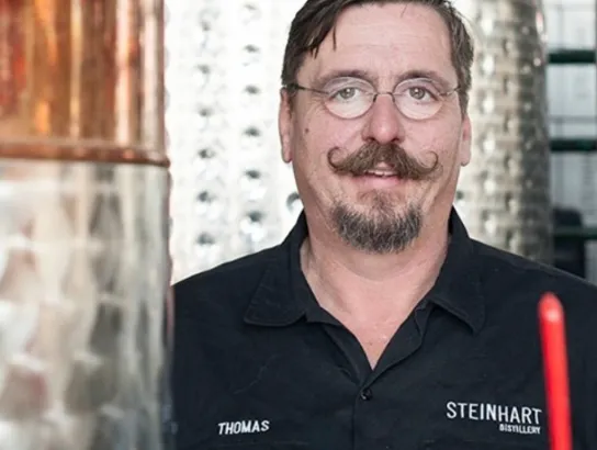 Owner of Steinhart Distillery standing in front of silver and copper distilling equipment