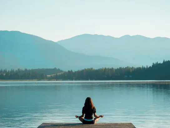 Woman meditating on a dock in front of a lake and mountains