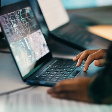 Hands typing, laptop and closeup on table of military intelligence, map and research on internet. Computer, soldier and veteran online for surveillance, cyber security and info of army professional