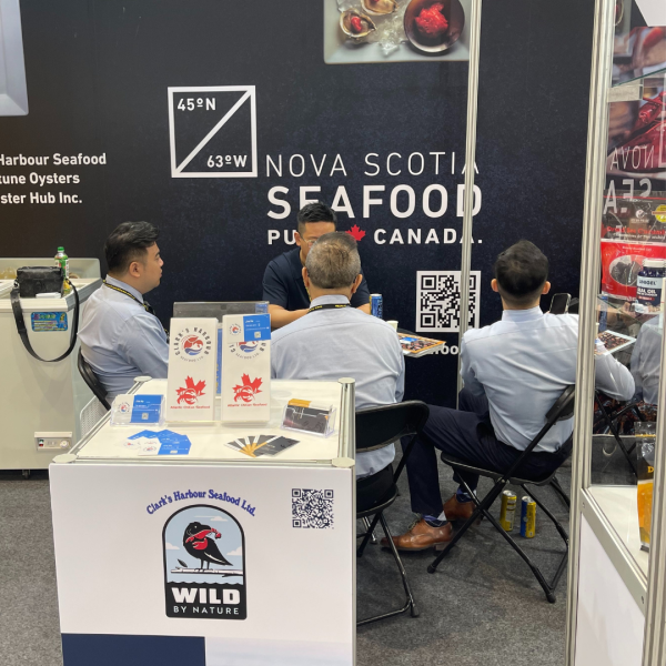 Food show exhibiting Clark's seafood with four men seated at table in backgrounf