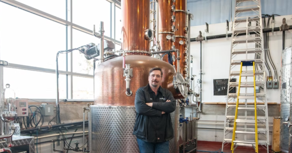 Man standing in front of distilling machinery