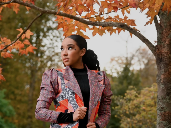 Woman in colorful coat posing under a tree with fall leaves
