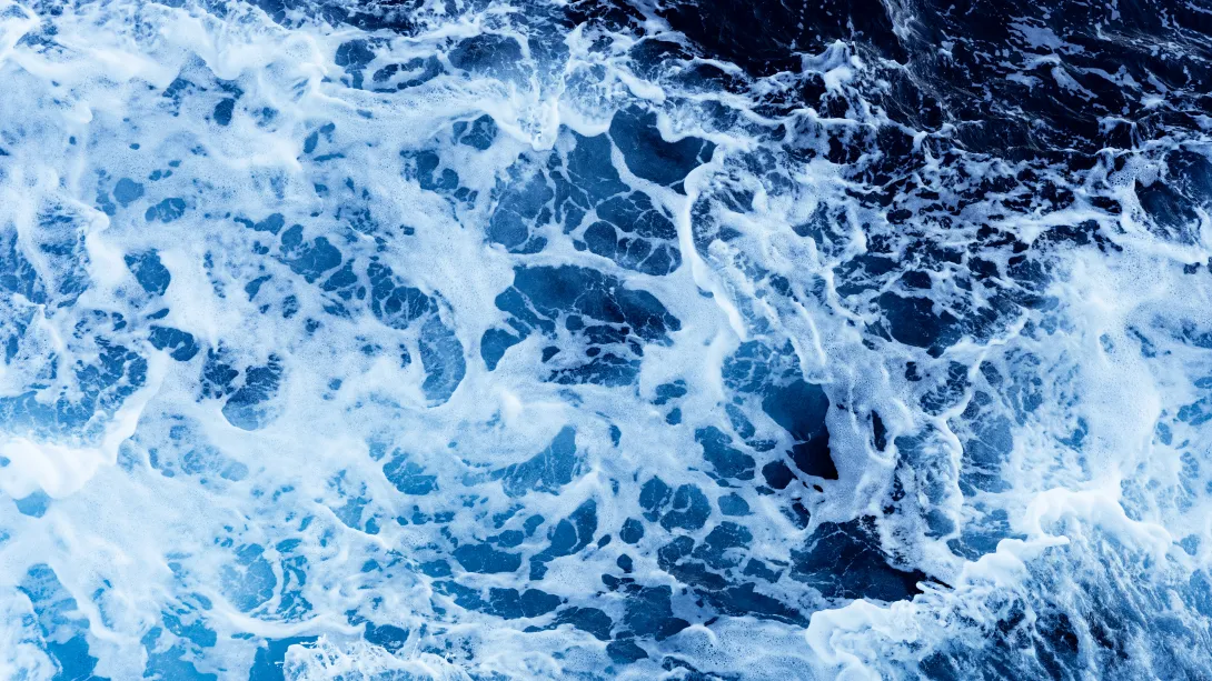 Deep blue ocean water with turbulent waves forming white foam and moving currents